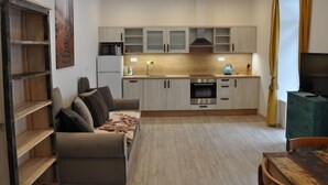 Een moderne keuken met inbouwapparatuur, een eethoek met een tafel en stoelen, en een zithoek met een bank en planken.