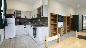 A modern kitchen with white cabinets, a microwave, a stove, and a sink. There is a dining table with chairs and a wooden bookshelf. - Rašeliniště by Interhome (Desná v Jizerských horách)