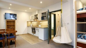 A compact room with a kitchenette, a dining area with a table and chairs, a hanging chair, and a bed with a checkered blanket. - Vodopády Černá Desná by Interhome (Desná v Jizerských horách)