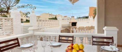 A dining area with a table set for four, a bowl of fruit, and a view of the surrounding neighborhood.