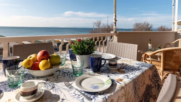 Mesa para dos con vistas al mar, un frutero y una planta en maceta en un balcón.