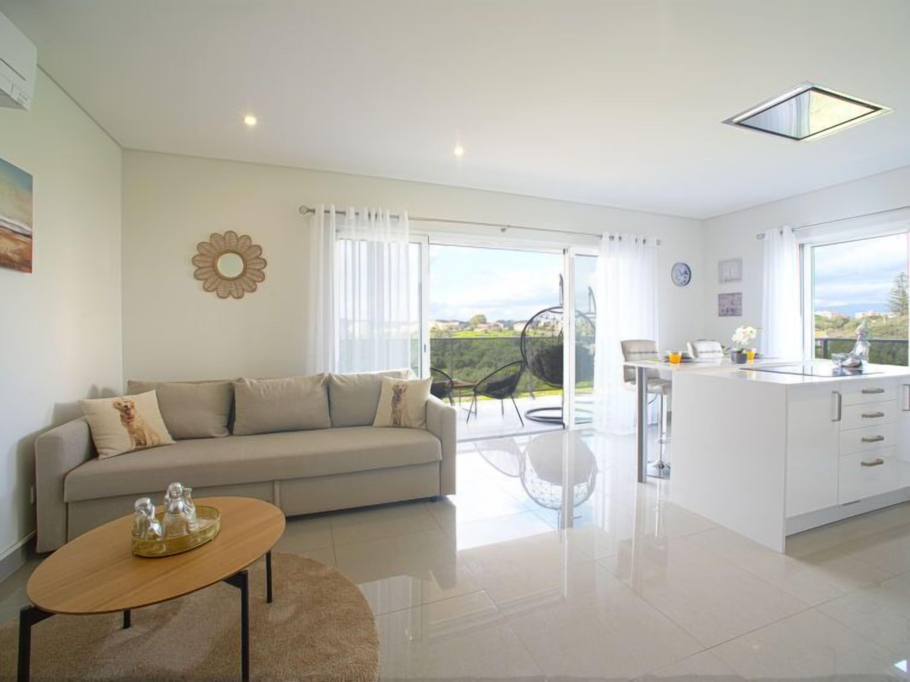A modern living room with a sofa, a coffee table, and a dining area with a kitchen counter.