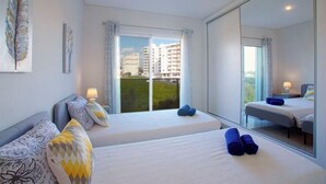 Moderni hotellihuone, jossa on kaksi sänkyä, suuri ikkuna ja näkymä rakennuksiin.