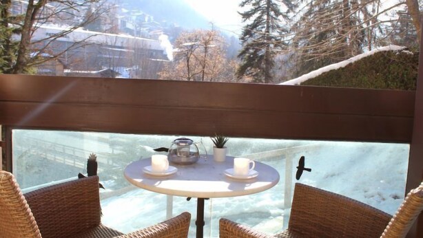 A balcony with wicker chairs and a table, overlooking a snowy landscape with trees and buildings. - Castel des Roches C4 by Interhome (Saint Gervais)