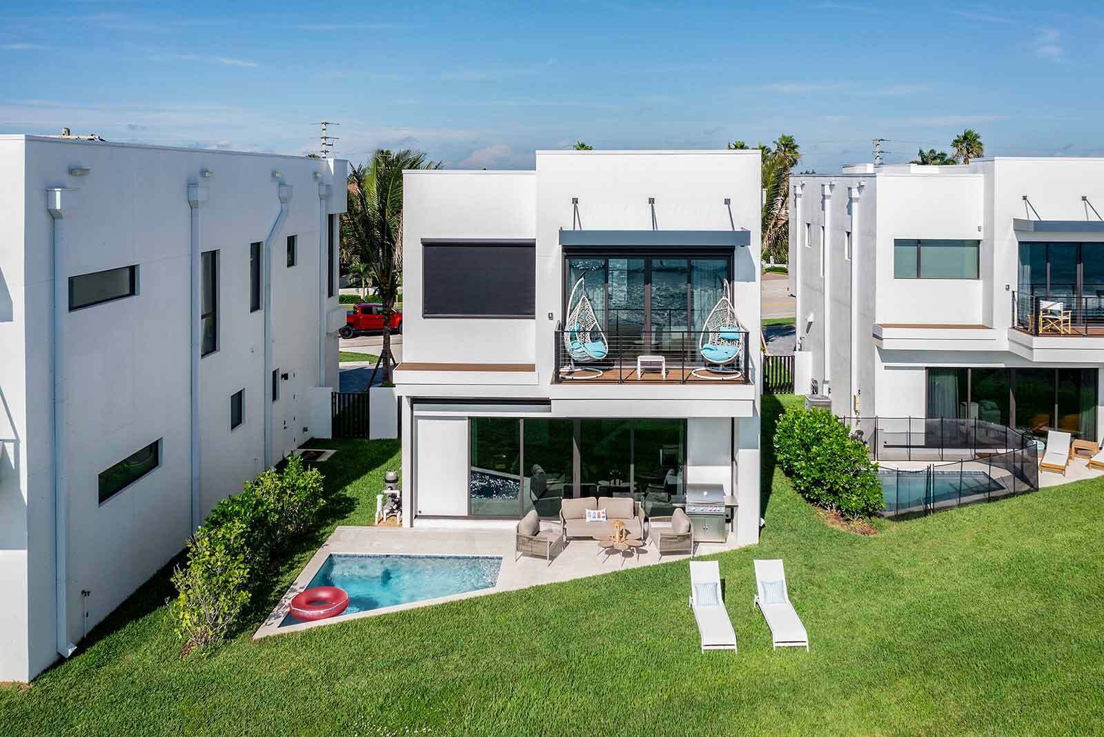 Una casa moderna de dos pisos con piscina, mobiliario exterior y un balcón con sillones colgantes.