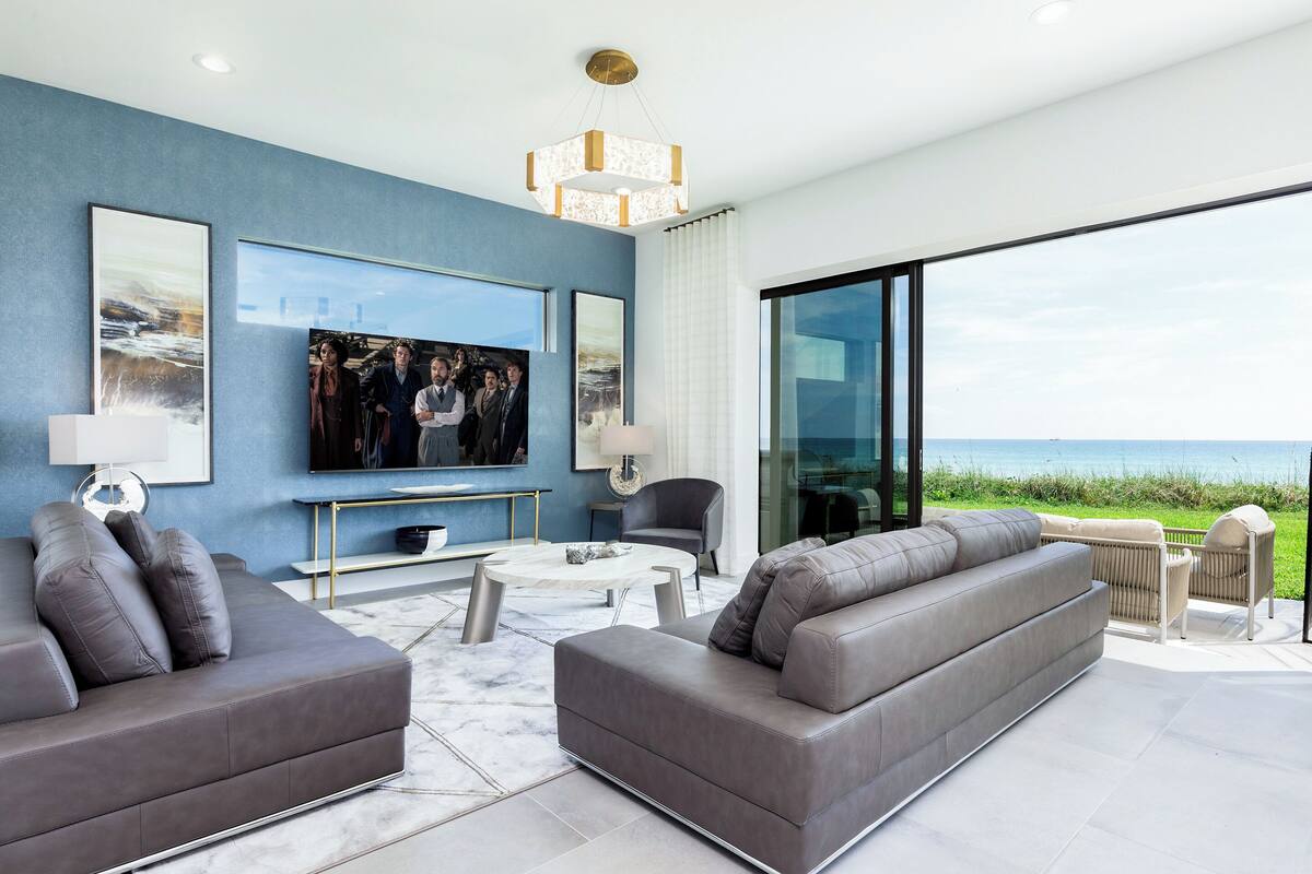 Ein modernes Wohnzimmer mit großem Flachbildfernseher, grauen Sofas, einem Couchtisch und Blick auf den Ozean.