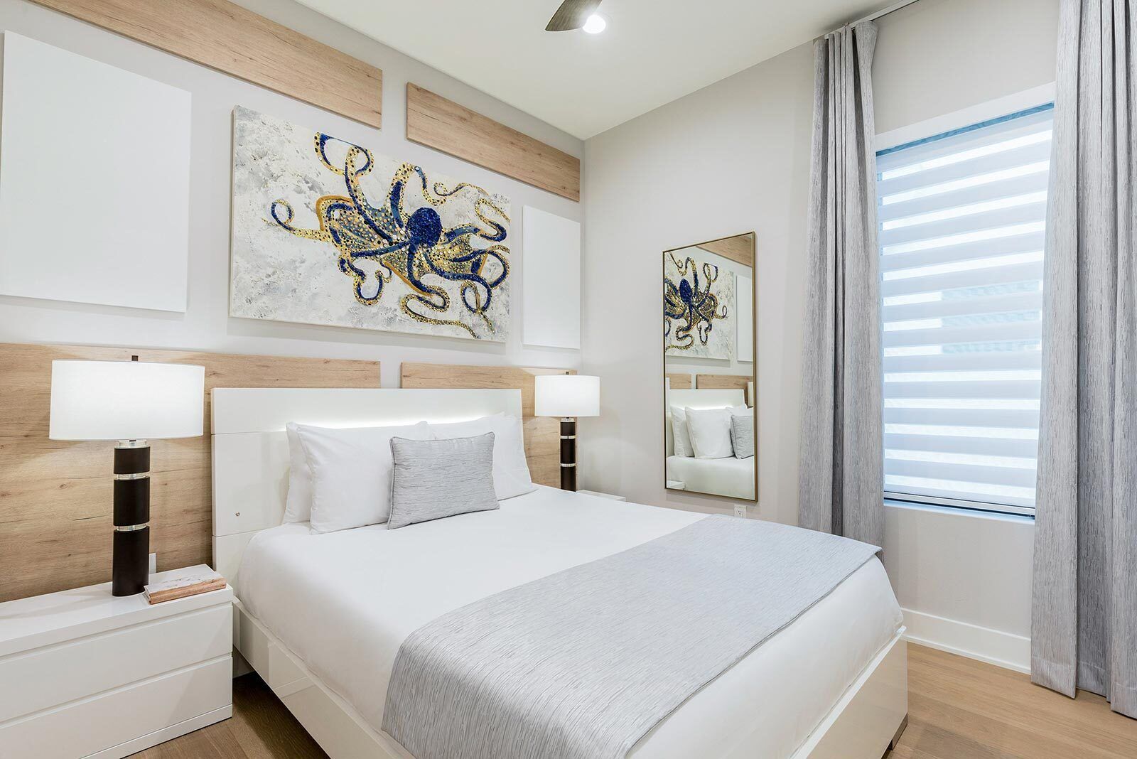 A modern bedroom with a large bed, two bedside tables, a mirror, and abstract wall art.