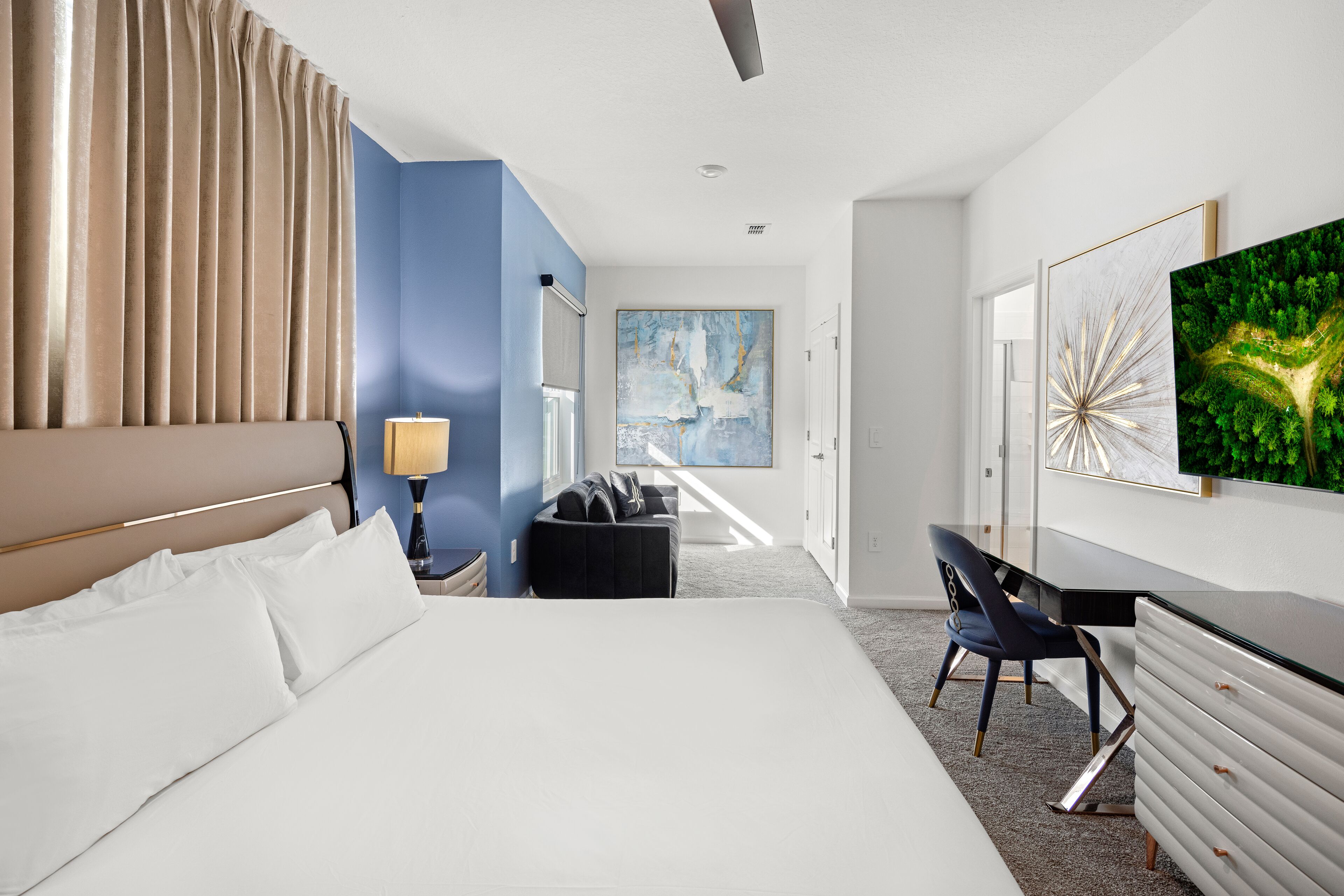 Una habitación de hotel con una cama grande, un escritorio, una silla, una lámpara y obras de arte en las paredes.