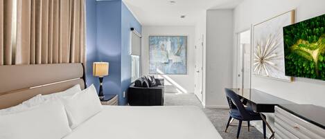 Una habitación de hotel con una cama grande, un escritorio, una silla, una lámpara y obras de arte en las paredes.