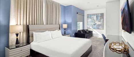 Une chambre d’hôtel moderne avec un grand lit, un ventilateur de plafond, un bureau avec une lampe et un tableau au mur.