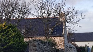 Une maison en pierre avec un toit en pente, un mur de pierre et un chemin qui y mène.