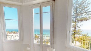 Ein Zimmer mit zwei weißen Stühlen, einer großen Schiebeglasdoor und Blick auf das Meer.