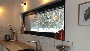A modern kitchen with a wooden countertop, a built-in sink, a window with a view of snow-covered trees, and a scale. - Wäller Haus - Design home with fireplace & private fenced garden (Breitscheid)