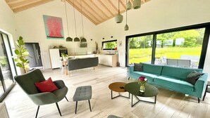 A spacious living area with a sofa, chairs, a coffee table, and a dining area with a kitchen in the background. - Wäller Haus - Design home with fireplace & private fenced garden (Breitscheid)