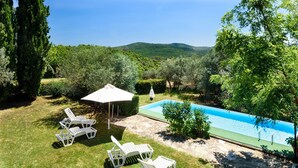 Un patio trasero con piscina, tres sillas reclinables blancas y un pergolado con sombrilla blanca.