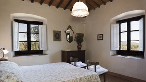 Un dormitorio con una cama, dos ventanas, un aparador, un espejo y una lámpara colgante.