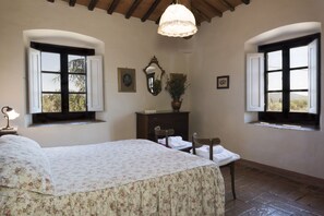 Una camera da letto con un letto, due finestre, una cassettiera, uno specchio e un lampadario.