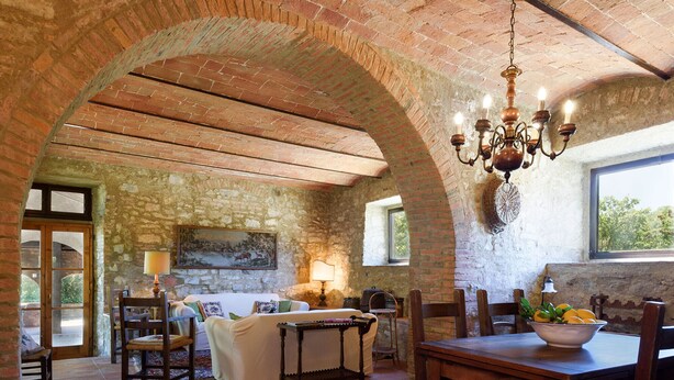 Un comedor rústico con un arco de ladrillo, muebles de madera y una araña.