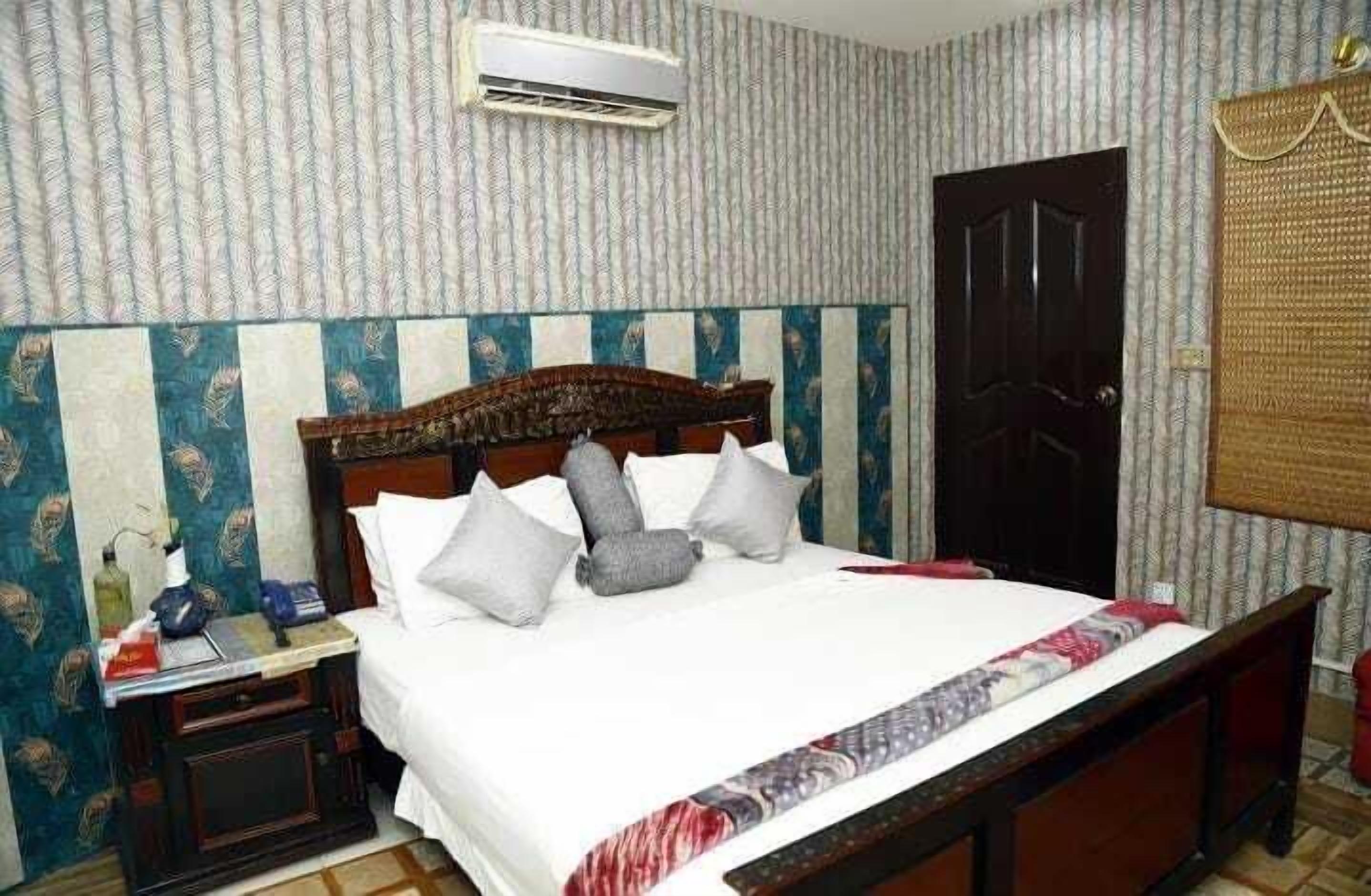 A neatly made bed with a wooden headboard, a bedside table with a lamp, and a patterned wall.