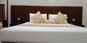 A neatly made bed with white linens and beige pillows, a wooden headboard, and a small nightstand with a phone. - Hotel New Holiday (Lahore)