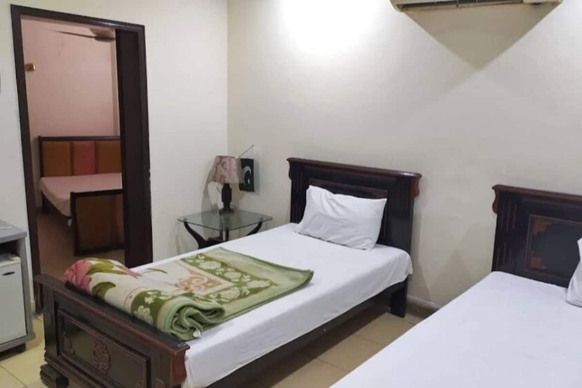 A room with two beds, a small table with a lamp, a mirror, and a door leading to another room.