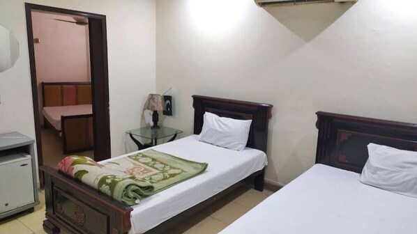 A room with two beds, a small table with a lamp, a mirror, and a door leading to another room. - Hotel New Holiday (Lahore)