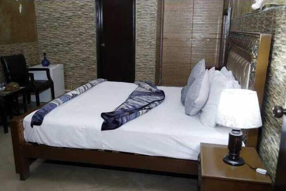 A neatly made bed with a white duvet and a patterned throw, a bedside lamp, and a chair in a room with textured walls and a wooden door.