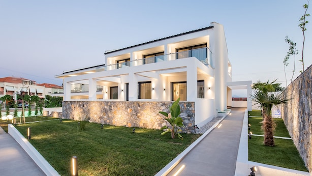 Una moderna casa a due piani con facciata in pietra, un balcone e un prato curato.
