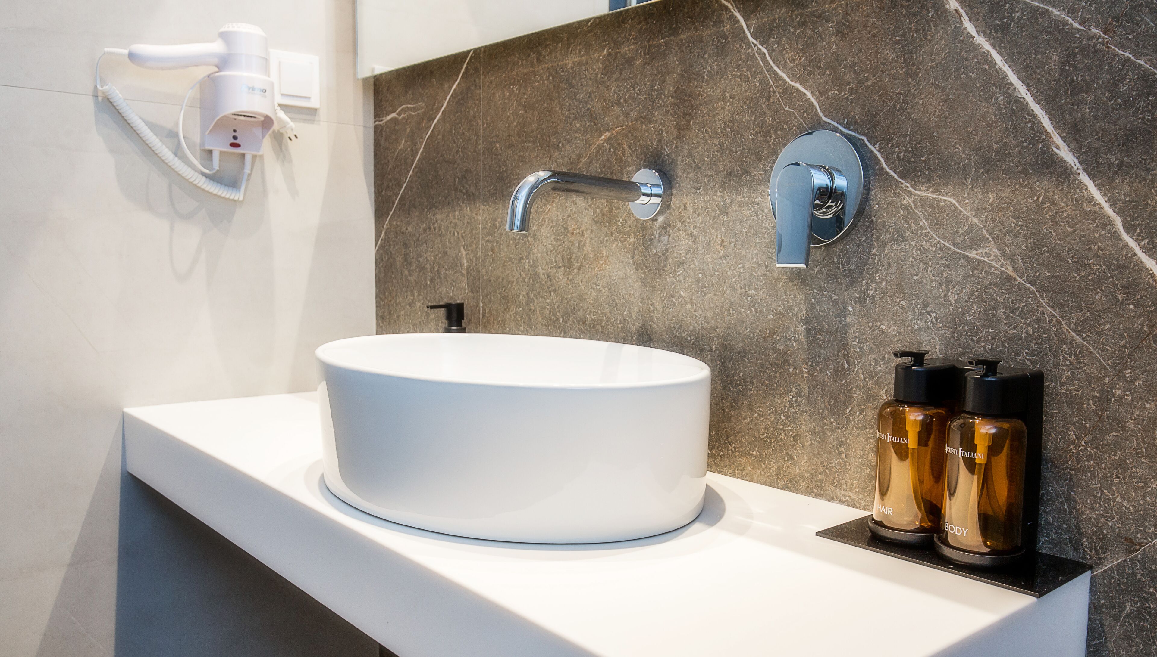 A bathroom with a white sink, a modern faucet, and two bottles of hair and body care products on the counter.