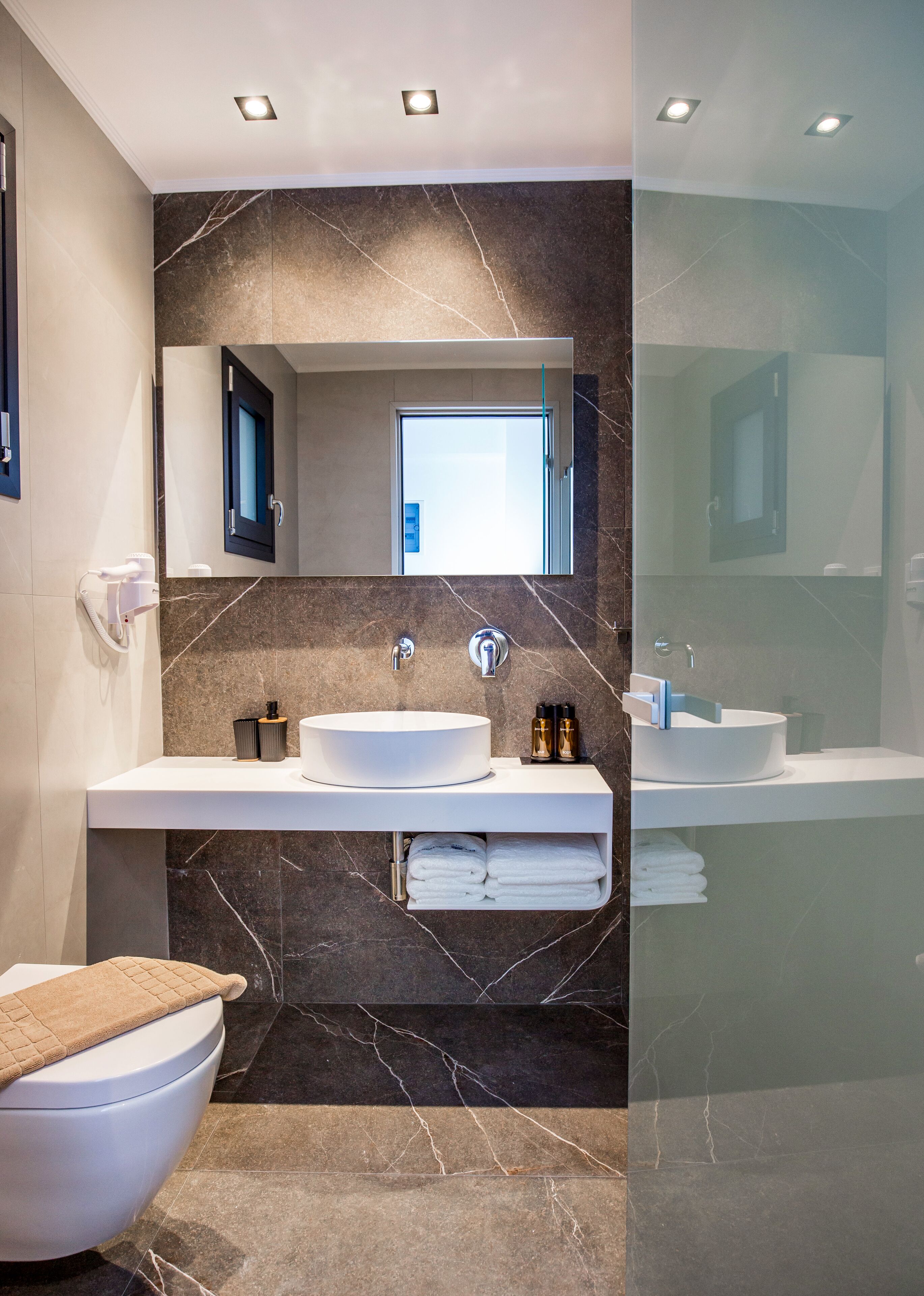 A modern bathroom with a large mirror, two sinks, and a toilet.