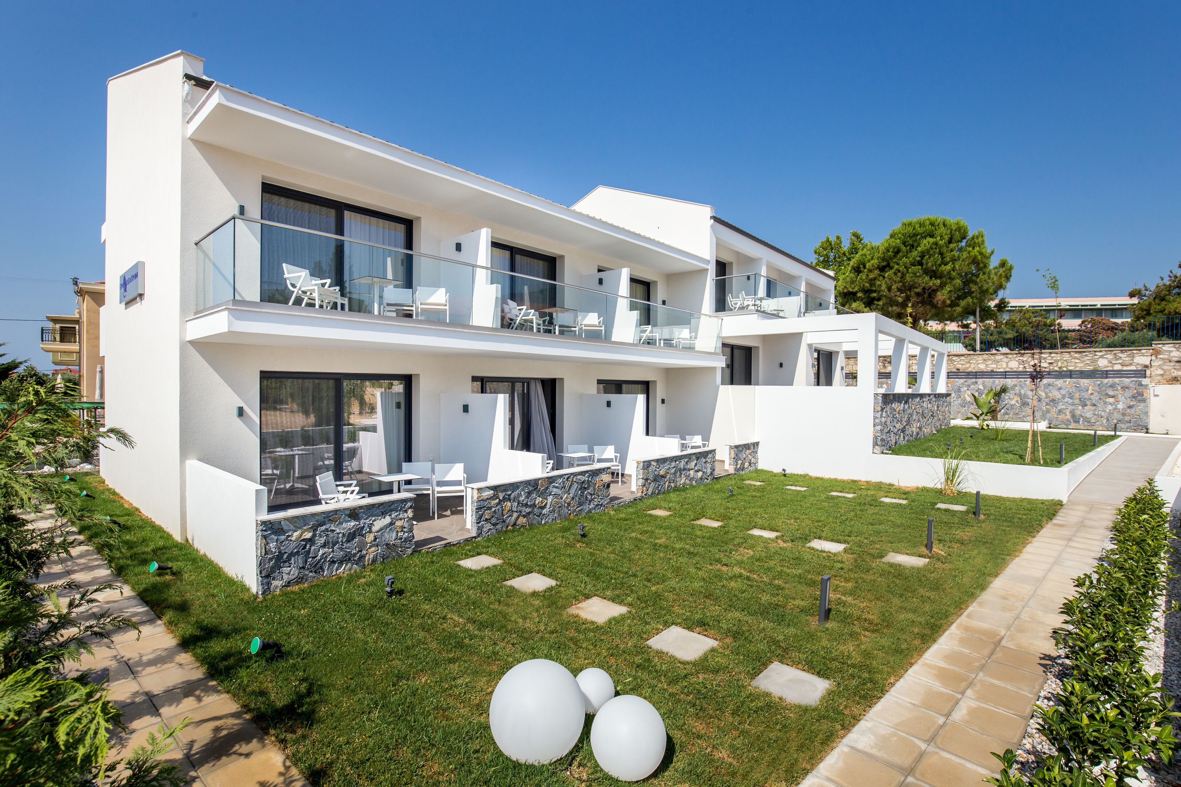 Une maison moderne à deux étages, dotée d’un balcon, d’un mur en pierre et d’une pelouse bien entretenue.