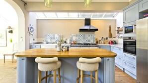 A modern kitchen with a central island, two bar stools, a built-in oven, and a microwave. - Cayenne Canopy, by Veeve (London)