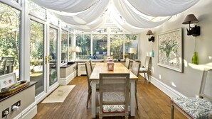A dining area with a wooden table, wicker chairs, and a chandelier. - Cayenne Canopy, by Veeve (London)