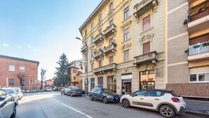 A street view with parked cars, a building with balconies, and a clear sky.