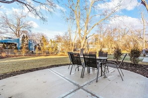 An outdoor patio with a table and chairs, surrounded by trees and a lawn.