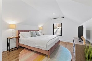 Una camera da letto con un letto, lampade da comodino, una TV, una finestra e una pianta.
