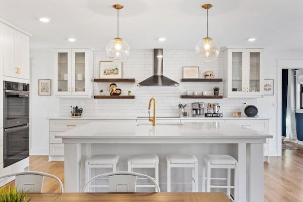 A modern kitchen with white cabinetry, a central island with stools, pendant lighting, and a stainless steel range hood.