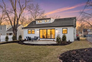 A two-story house with a covered patio, a large sliding glass door, and a small front yard with a lawn and a tree.
