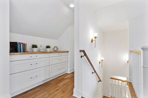 Un escalier avec une rampe blanche et des appliques murales, menant à un palier doté d’un mur blanc et d’un plancher en bois.