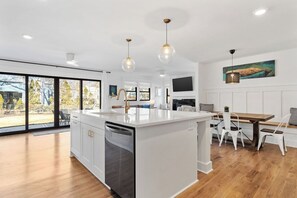 Une cuisine moderne dotée d’un îlot central, de meubles blancs et d’un coin repas avec une table et des chaises en bois.