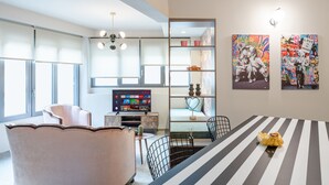 A modern living room with a large TV, a dining table with chairs, and a sofa. - Acropolis Pop Art Apartment (Athens)