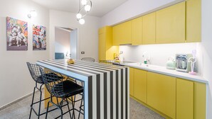 A modern kitchen with yellow cabinets, a striped island, and black wire chairs. - Acropolis Pop Art Apartment (Athens)