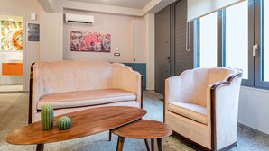 A modern living room with a beige sofa, a matching armchair, and a small wooden coffee table with two decorative vases. - Acropolis Pop Art Apartment (Athens)