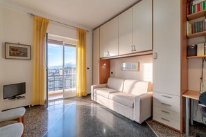 Ein modernes Wohnzimmer mit einer Couch, einem Fernseher, einem Bücherregal und einer Glastür, die auf einen Balkon führt.