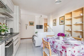 Una cocina moderna con electrodomésticos de acero inoxidable, un comedor con una mesa dispuesta para dos personas y un sofá blanco al fondo.