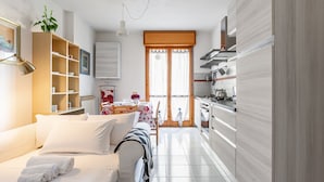 Quarto de hotel moderno com uma cama, uma pequena mesa de jantar, uma área de cozinha e uma janela grande.