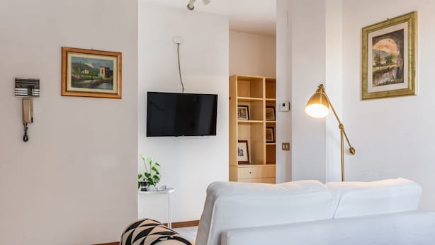 Quarto de hotel moderno com televisão de tela plana, luminária de cabeceira, sofá e estante de livros.