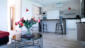 A modern kitchen with white cabinets, a microwave, and a coffee machine. There is a dining area with a glass table and chairs, and a vase with flowers on the table.