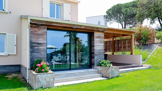 A modern house with a glass door, stone steps, and a wooden pergola.