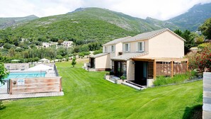 A modern house with a swimming pool, surrounded by lush green hills and mountains.